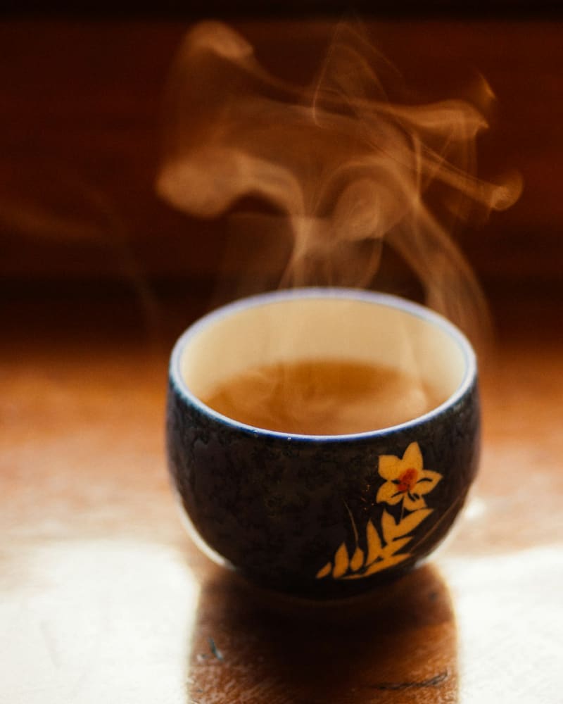 A cup of roasted green tea steaming on a dark timber table.