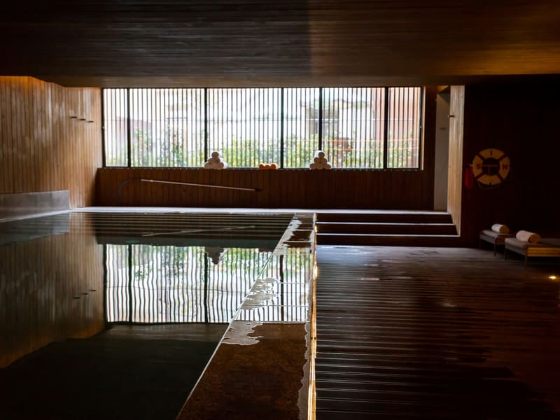 A timber-lined bathing room, the water reflecting a slatted window.