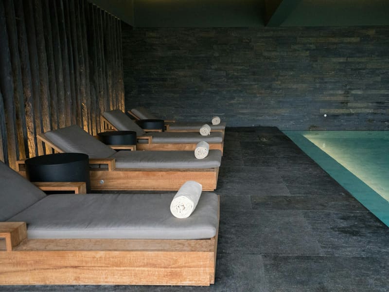 A quiet pool hall in dark stone, loungers set along the water.