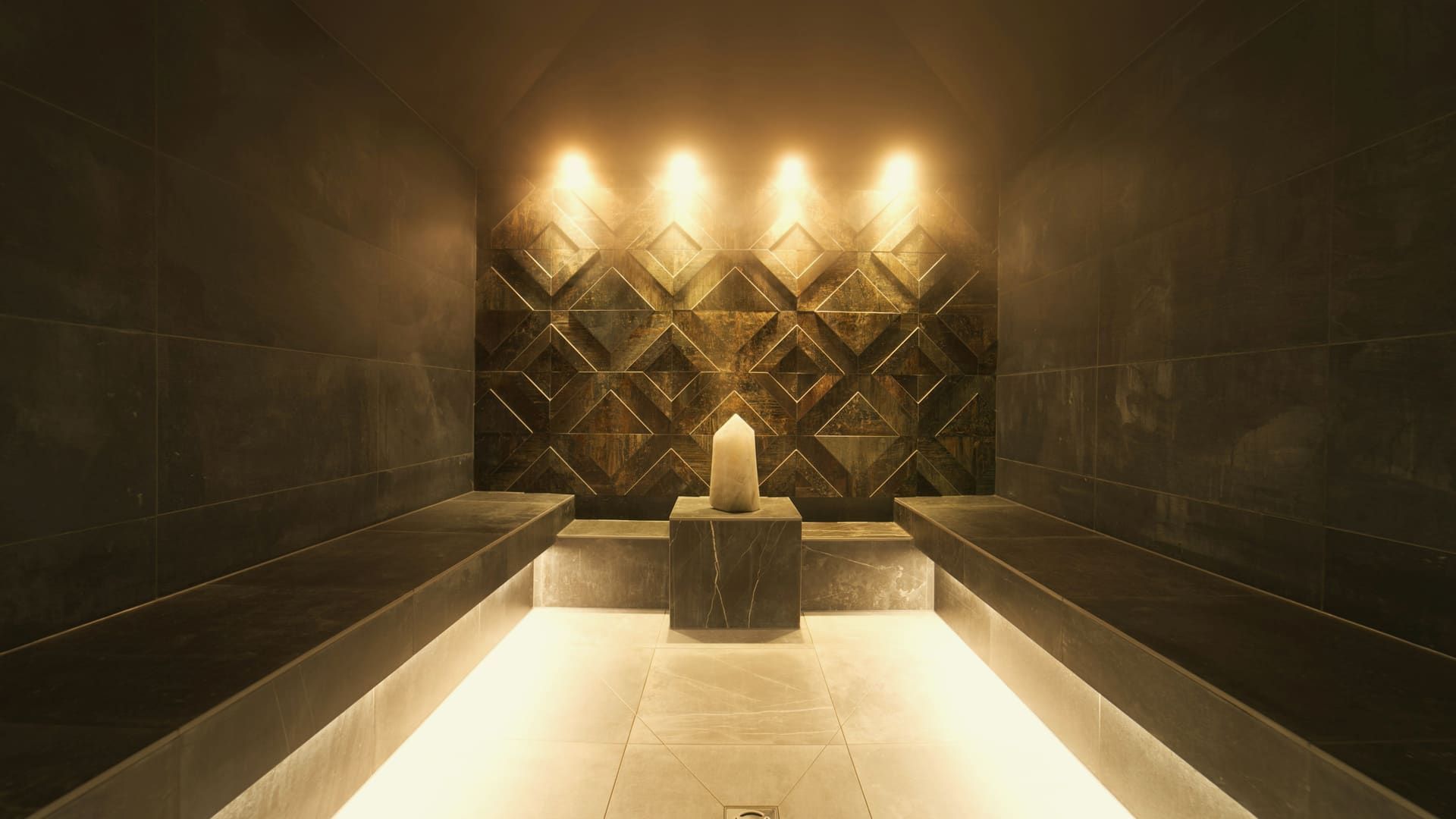A candlelit steam room, warm light running along its stone floor.