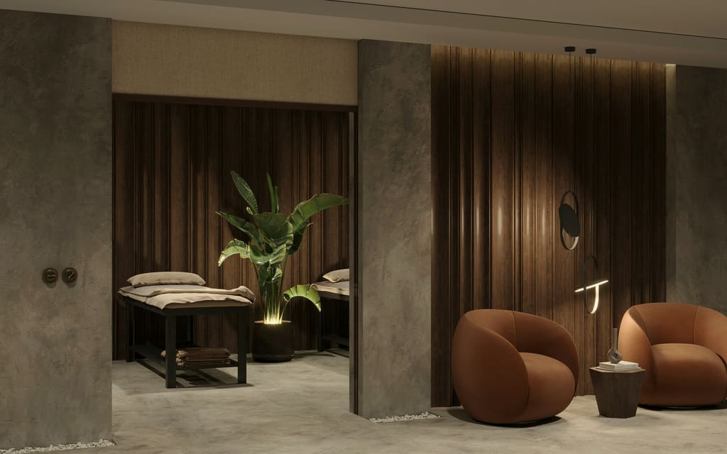 A quiet treatment suite in dark timber, a made bed and two armchairs set low.