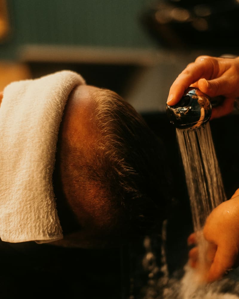 Warm water poured over a guest’s hair at the basin, a towel folded at the brow.